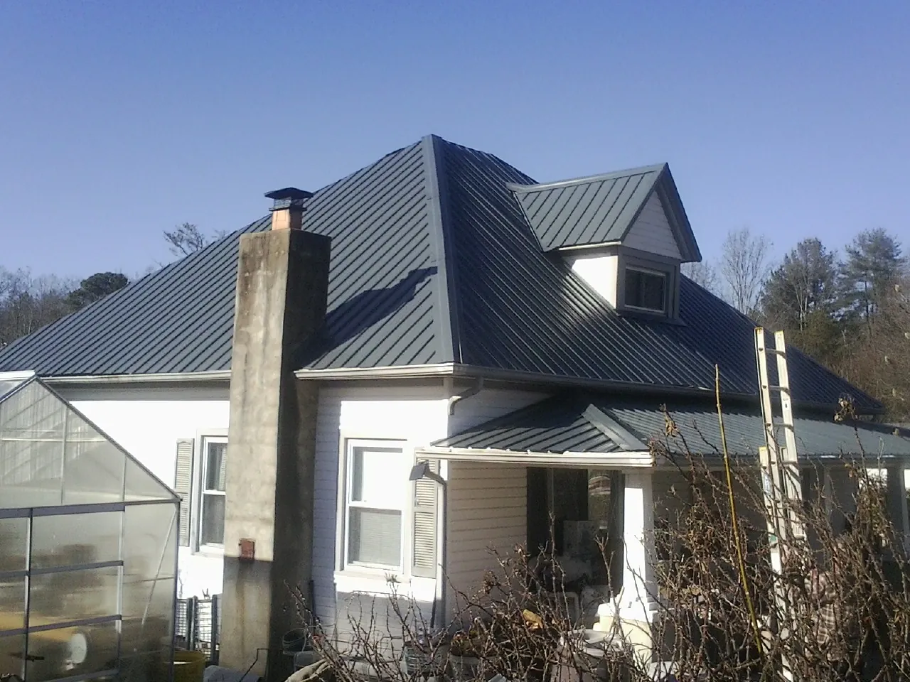 Dark blue standing seam metal roof on a white farmhouse with dormer — Slate & Tile Roof Repair by Roofing Brothers in West Granby