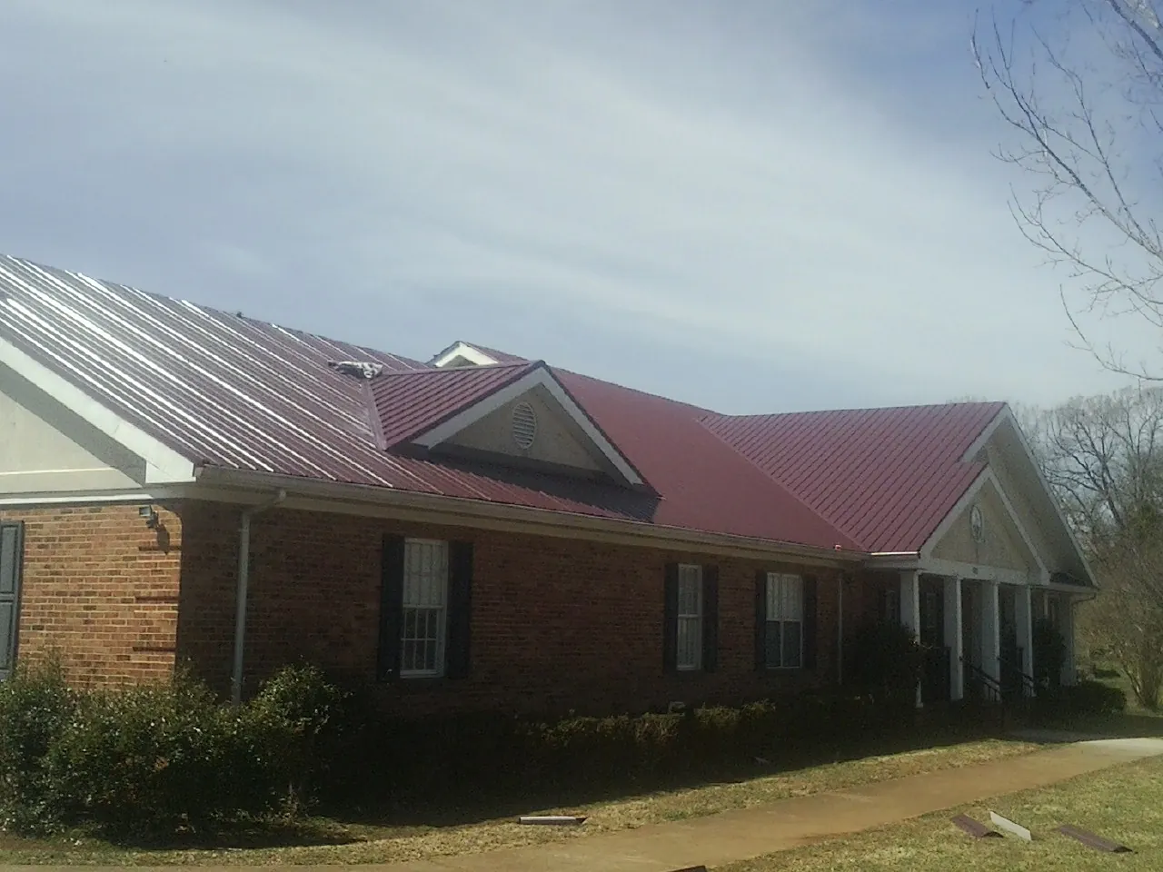 Red metal roof with gabled entries on a long brick building, from a Hail Damage Roof Repair job in West Granby
