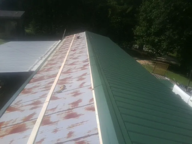 Old rusted panels beside newly installed green metal roofing — Wind Damage Roof Repair by Roofing Brothers in West Granby