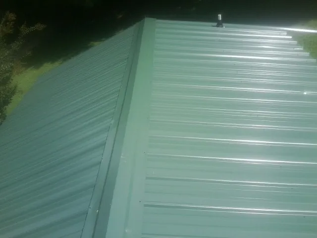 New green metal panels meeting at the ridge of a roof — Flat Roof Repair work by our crew in West Granby