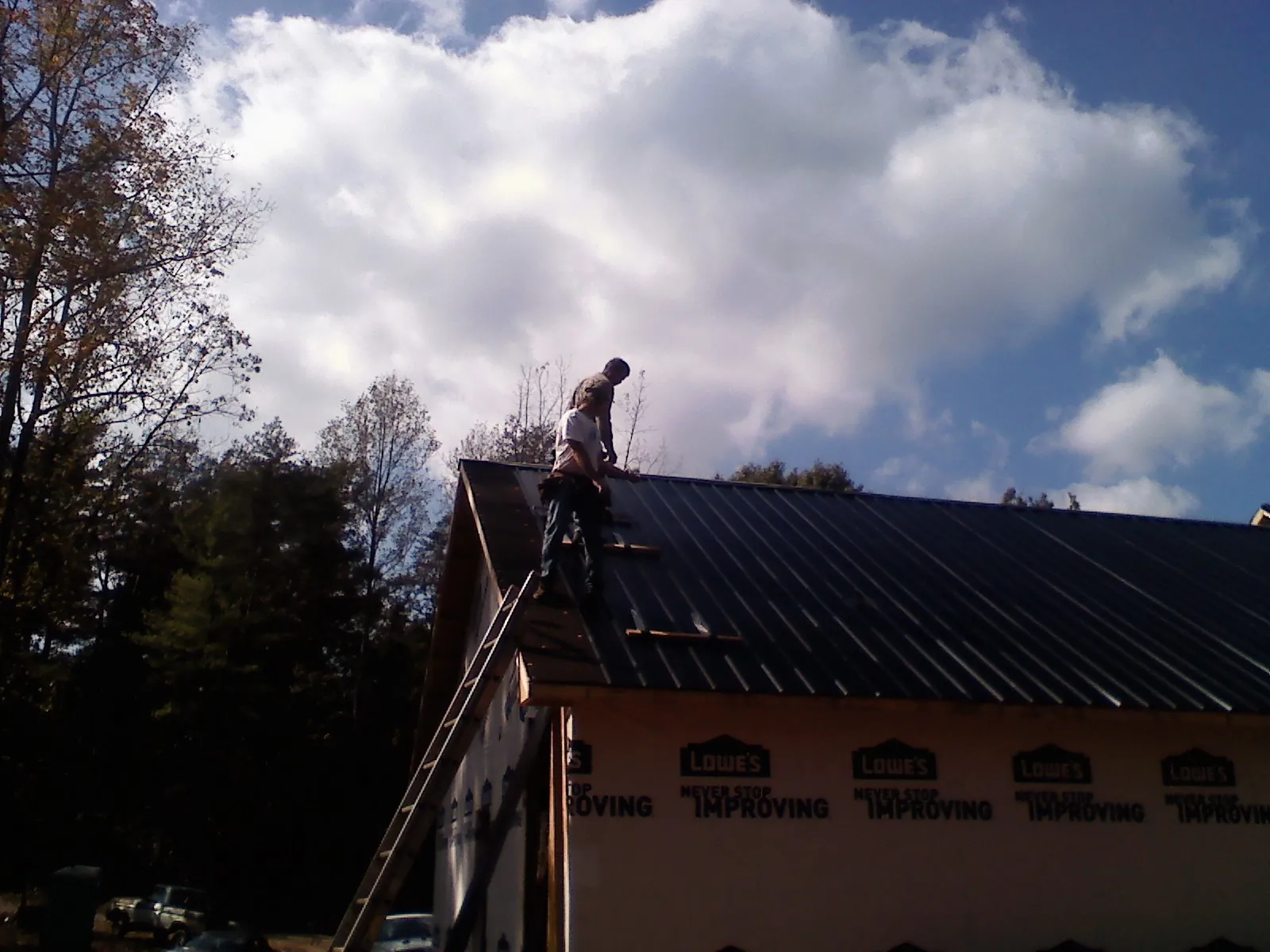 Roofer fastening dark metal panels high against a cloudy sky, from a Roof Inspection job in West Granby