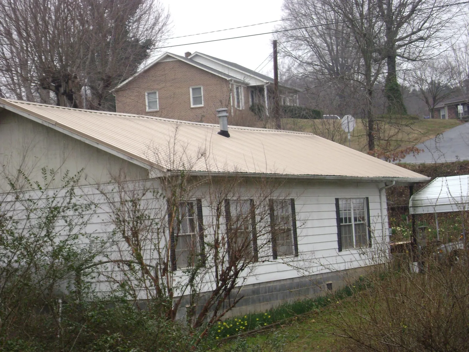 Tan metal roof on a white sided house set into a hillside — Commercial Roofing by Roofing Brothers in West Granby